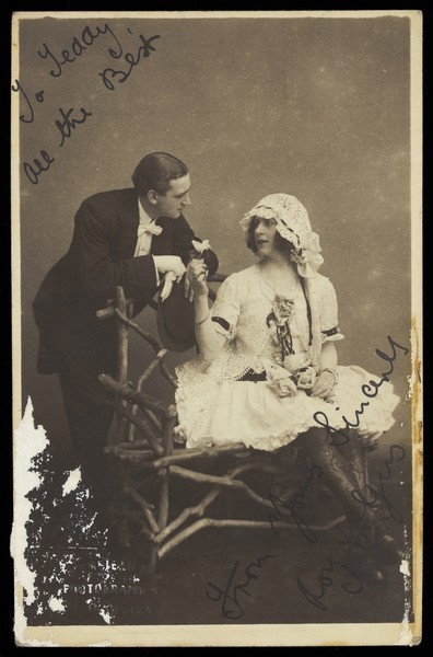 Download the full-sized image of Roy and Gus, two music-hall actors, one in drag, converse across a bench. Photographic postcard by Greenfield Bros, 192-.