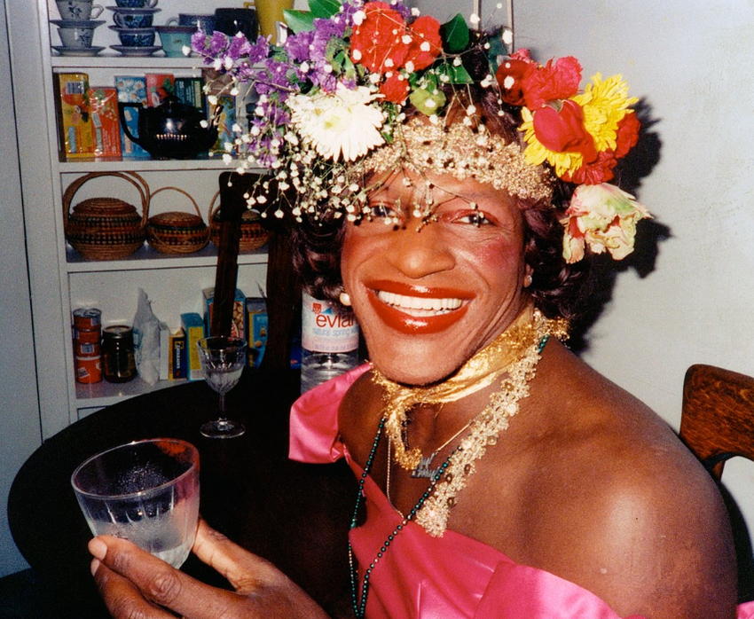 Download the full-sized image of A Photograph of Marsha P. Johnson Wearing a Hot Pink Top While Lifting a Glass and Smiling