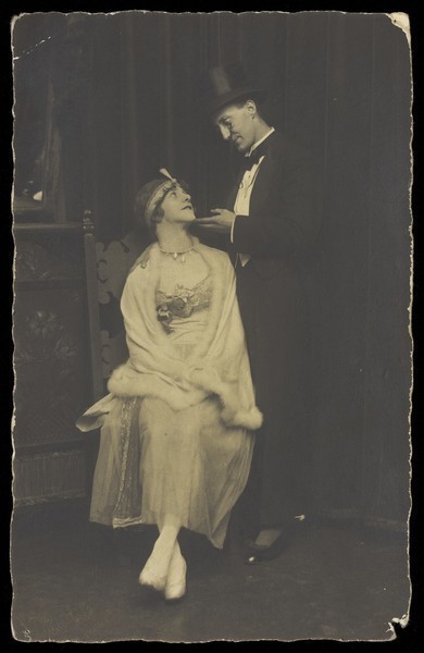 Download the full-sized image of Two actors pose on stage: a man wearing top hat and tails gazes down at a man in drag. Photographic postcard, 192-.