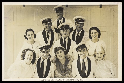 Download the full-sized image of Members of "Harry Gold's Margate Entertainers", one in drag, pose for a group portrait. Photographic postcard, 1937.